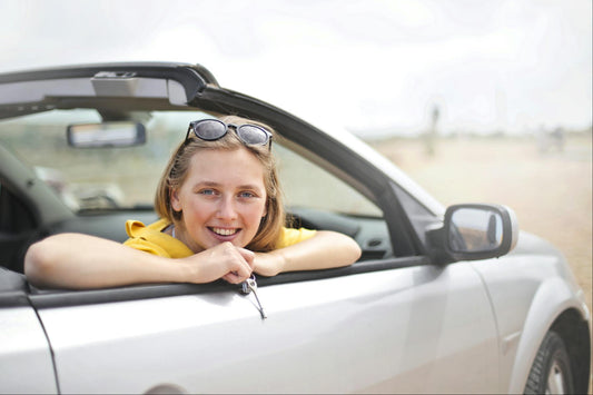 A female student holds the car keys with a proud smile, sitting in the driver's seat of a sleek white car. Ready to start her driving journey, she prepares for her next lesson with confidence and excitement.